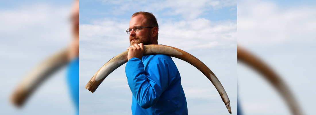 Man med glasögon håller en stor mamuttbete över axeln.